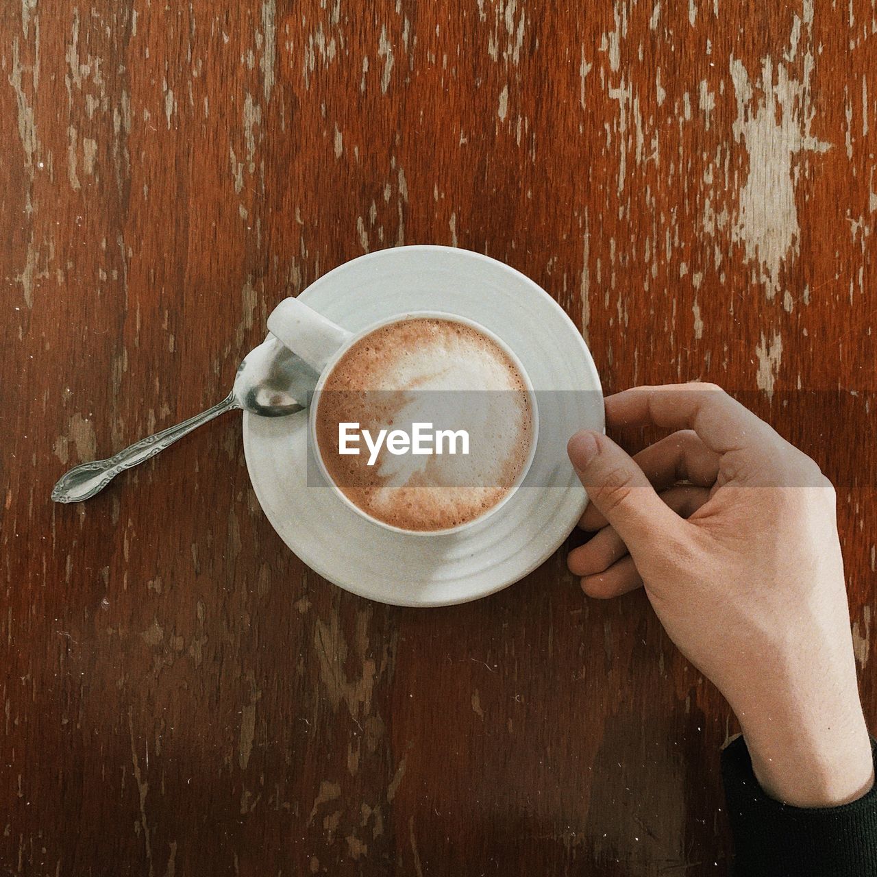 Cropped hand of person with coffee cup on wooden table