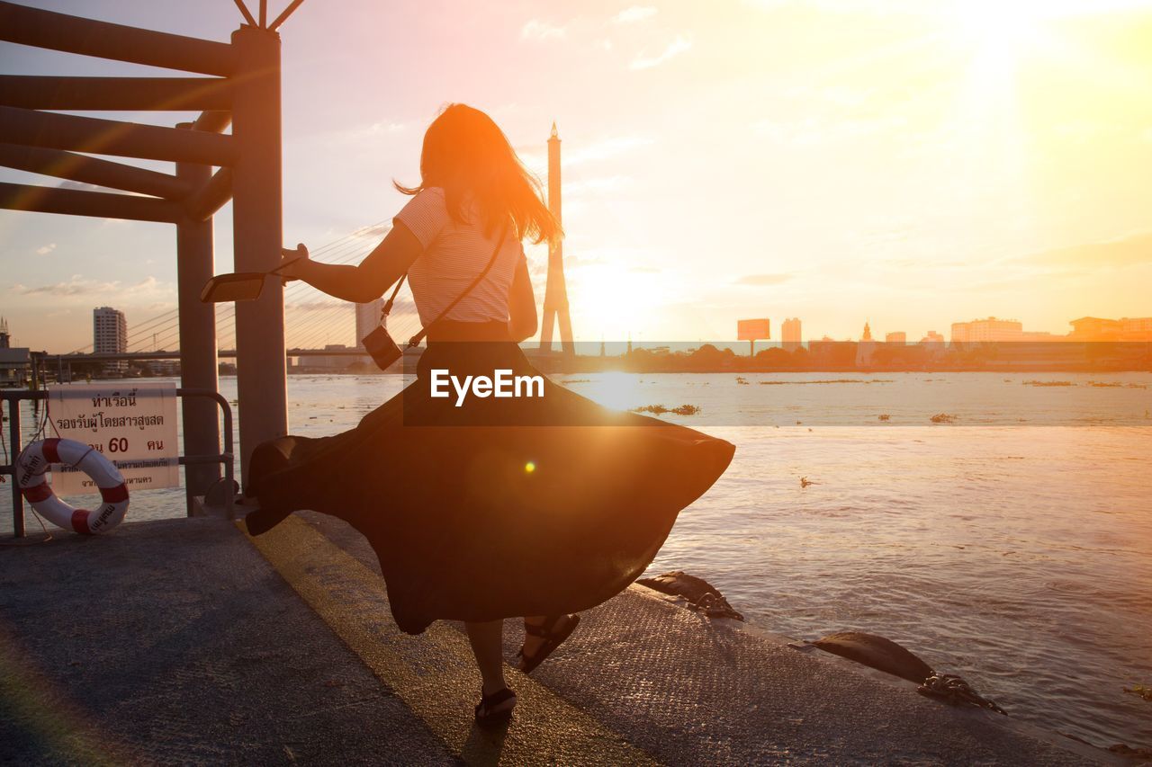 Rear view of woman standing by lake during sunset