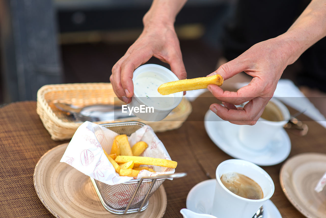 Midsection of man holding french fries with sauce in container over restaurant table