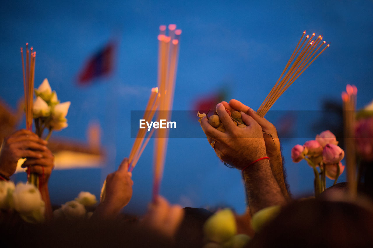 Cropped hands of people holding religious offerings against sky at dusk