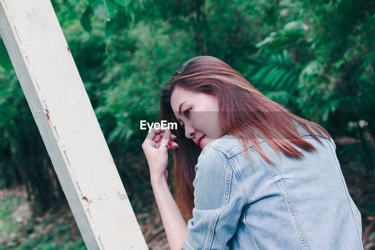 Rear view of beautiful woman looking away while sitting in forest