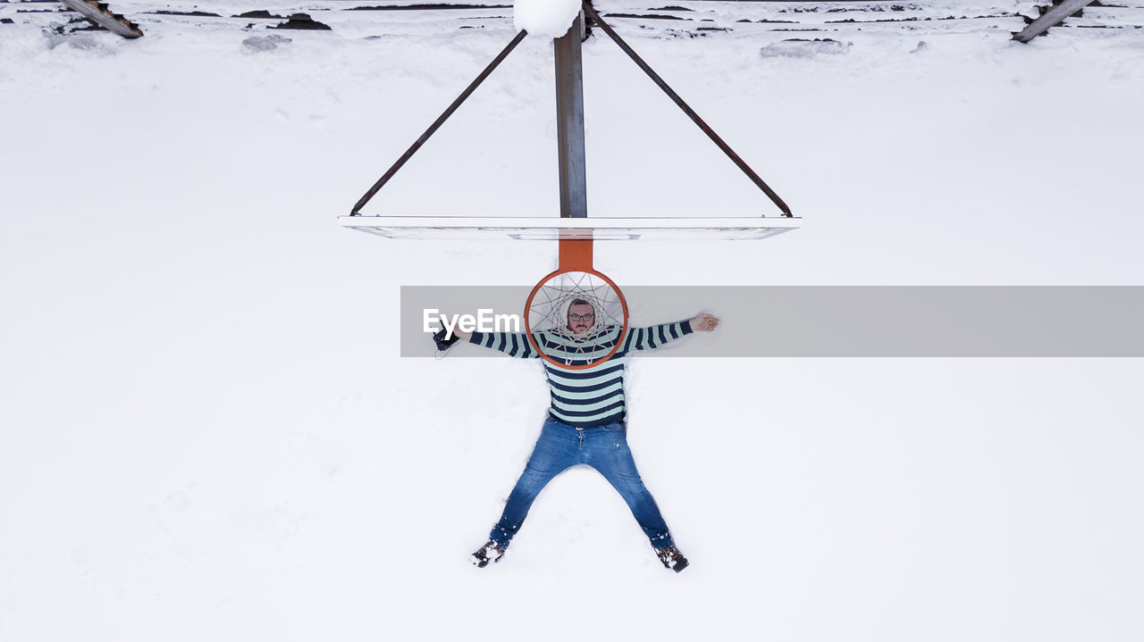 Directly above view of man lying on snow covered basketball court