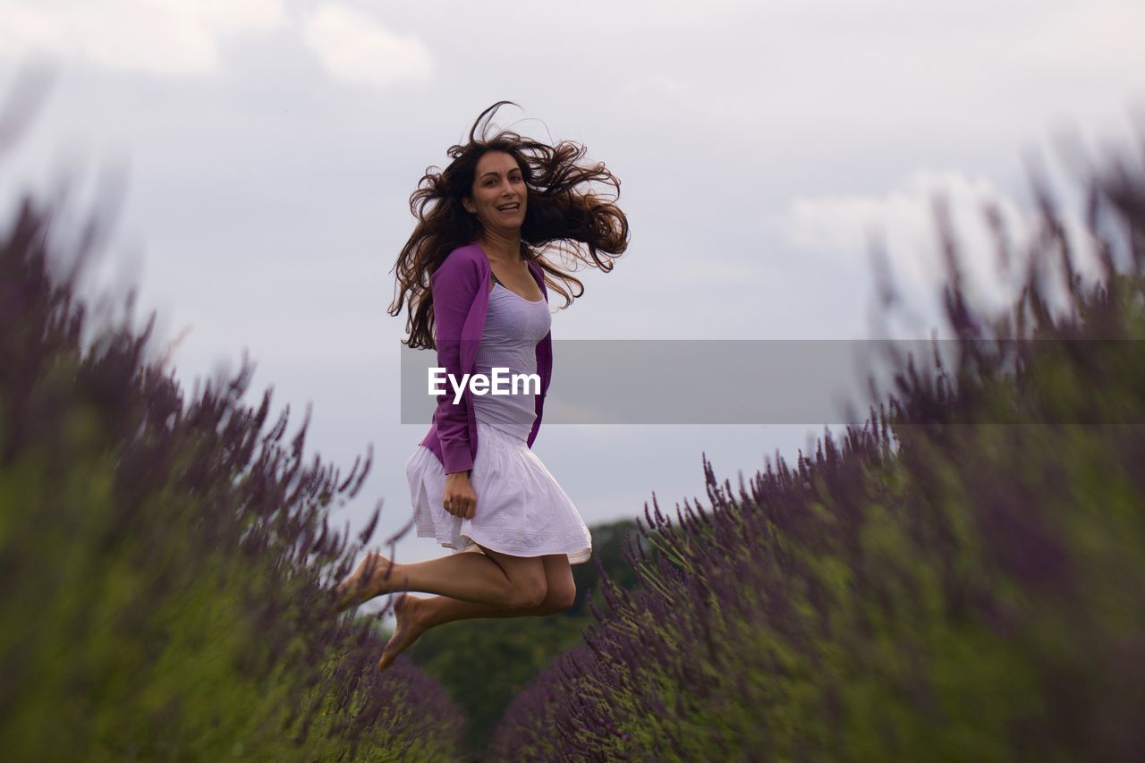 Full length portrait of happy woman jumping amidst lavenders