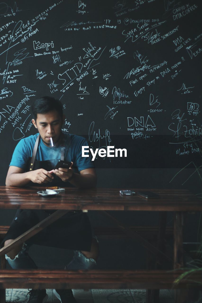 MAN USING MOBILE PHONE WHILE SITTING IN LAPTOP