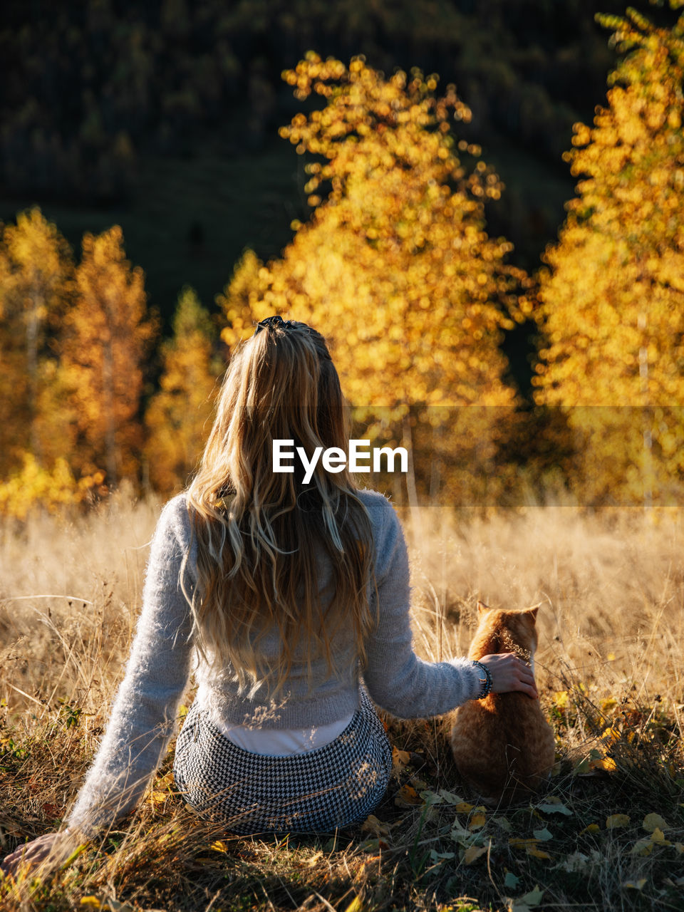 REAR VIEW OF WOMAN SITTING ON ROCK