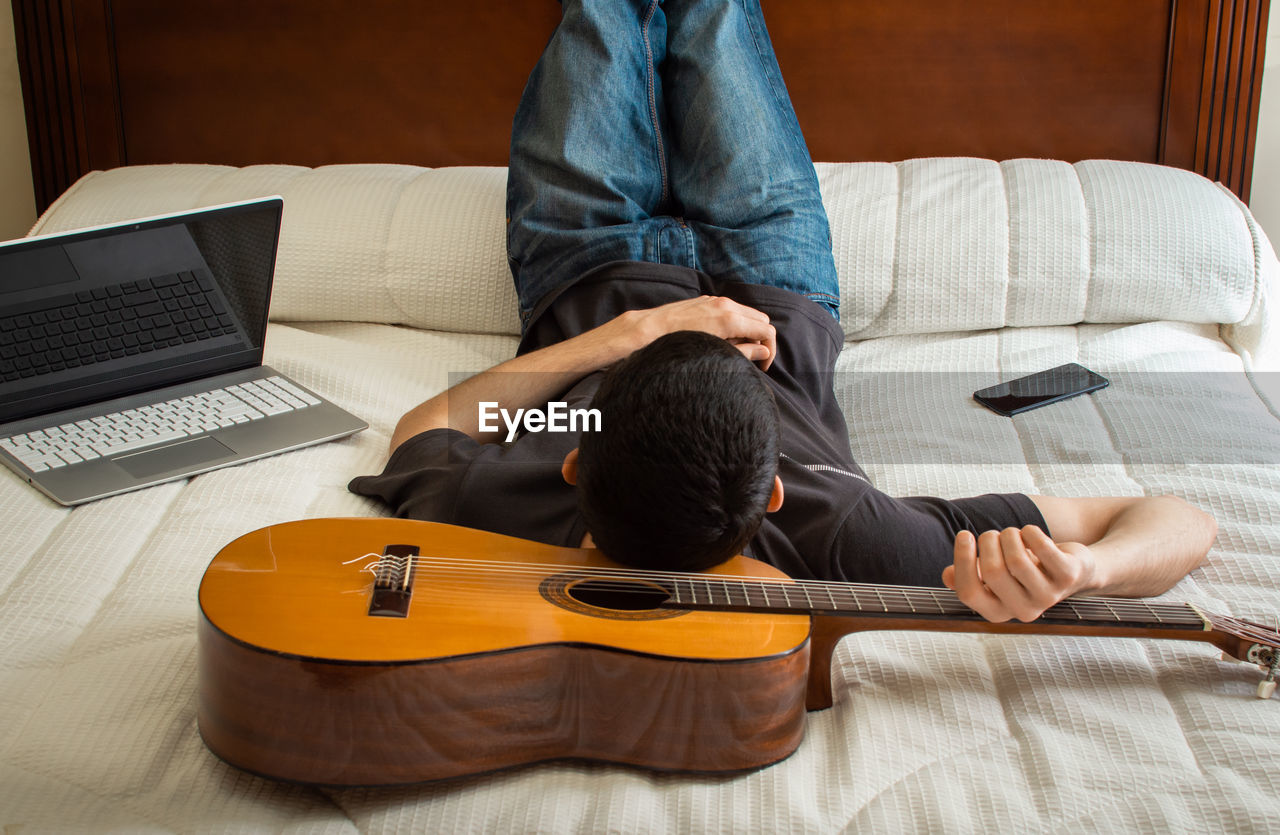 Man with guitar lying on bed at home