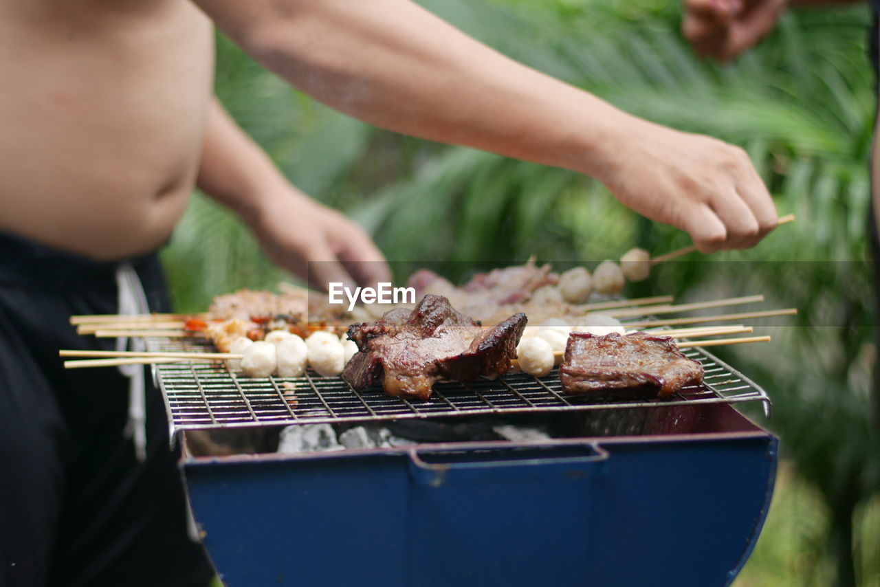 Midsection of shirtless man preparing food on barbecue grill