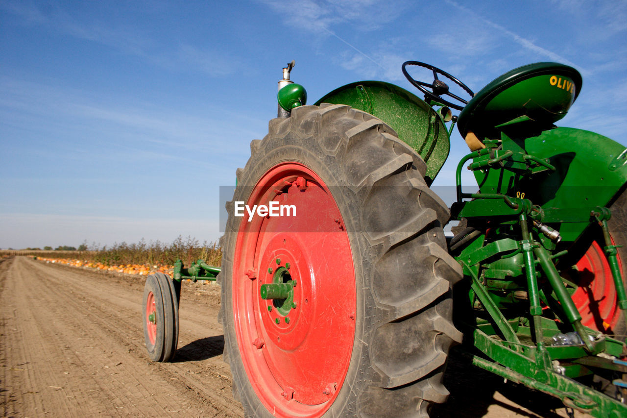 TRACTOR ON ROAD AMIDST FIELD AGAINST BLUE SKY