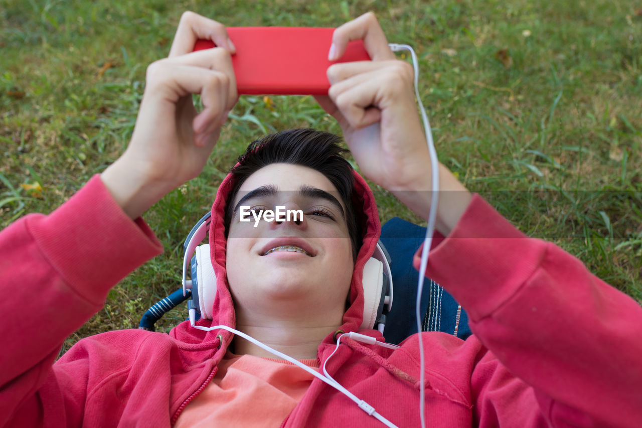 Top view portrait of young man with mobile phone and headphones lying in the field
