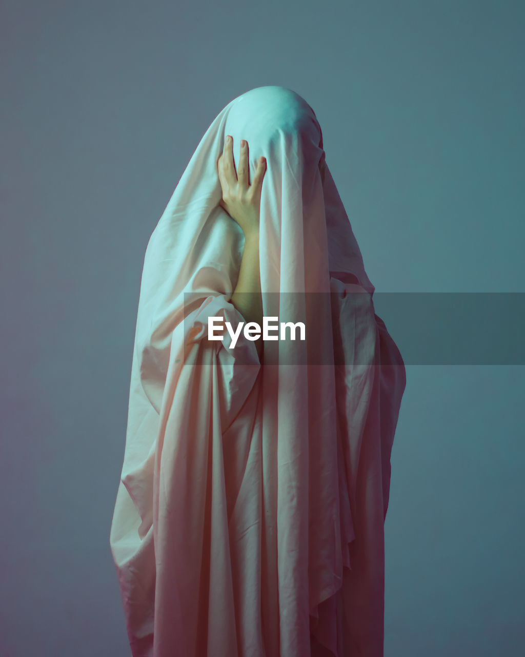 Scared woman hiding in textile against wall