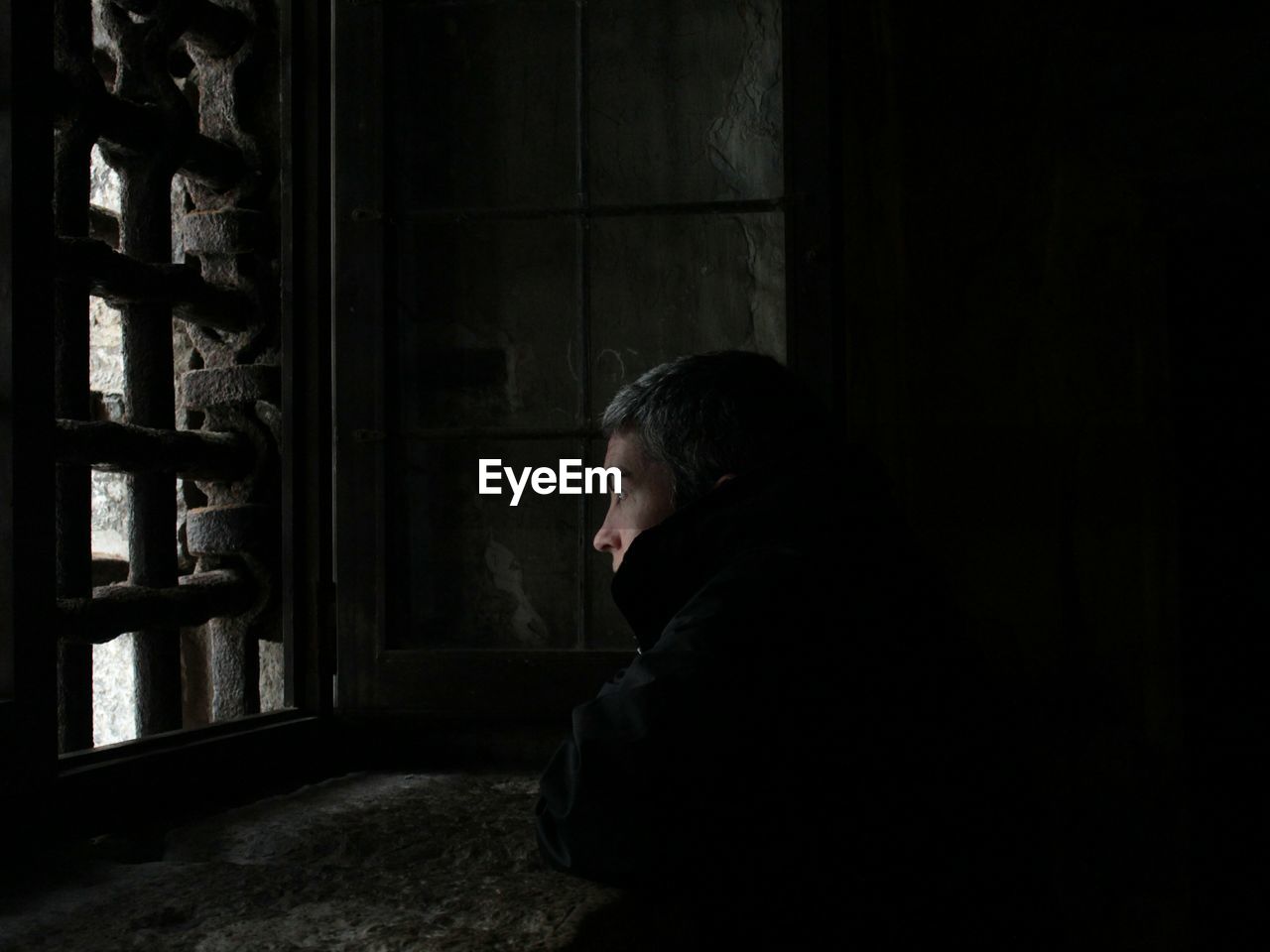 Side view of thoughtful man looking away while standing by window in prison