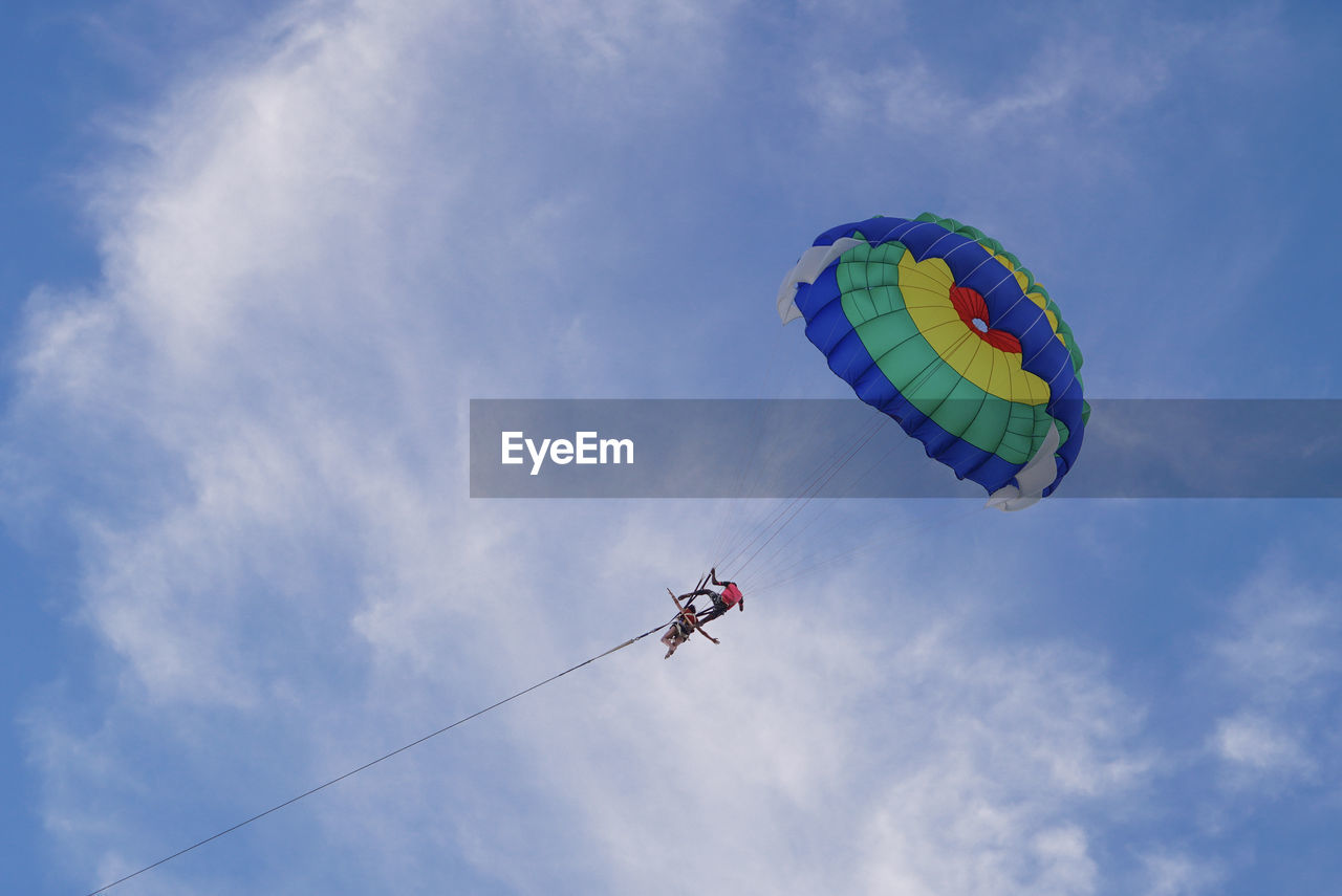 Low angle view of people parasailing against sky