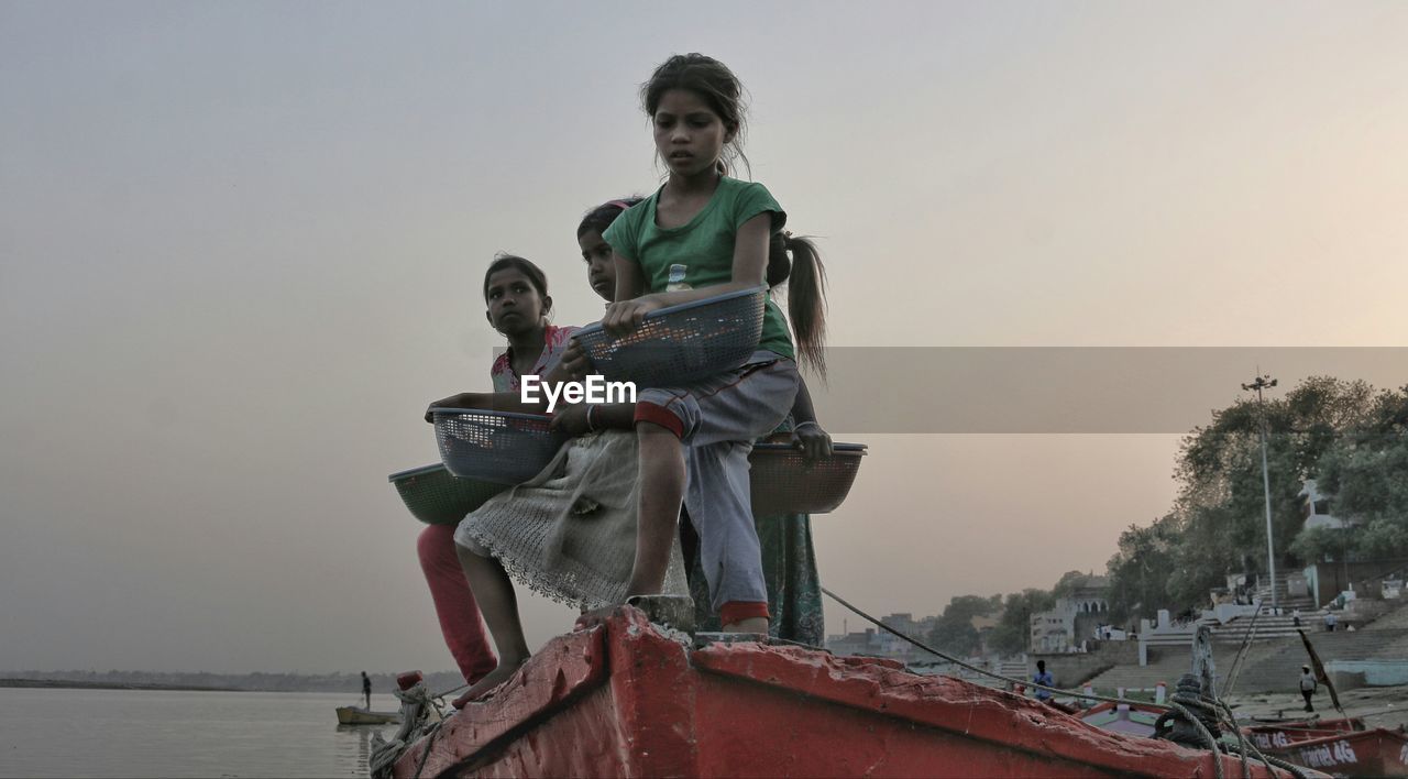 HIGH ANGLE VIEW OF WOMAN SITTING ON BOAT AGAINST SKY