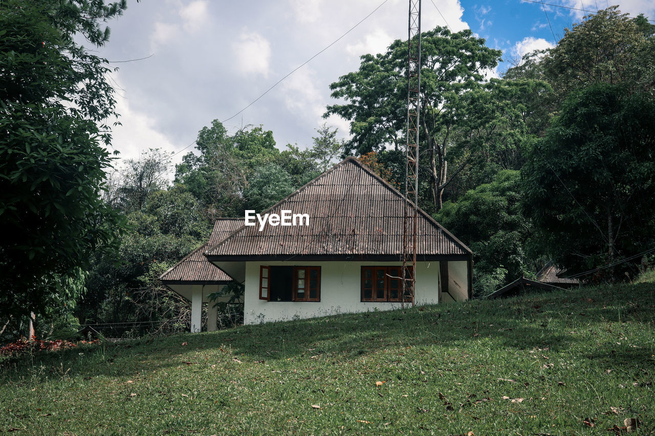 House on field by trees against sky