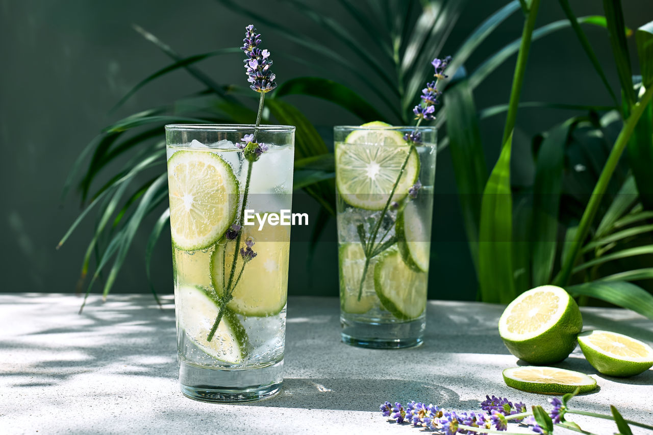 Cool lavender lemonade with lime slices and lavender flower on the table near dark green surface