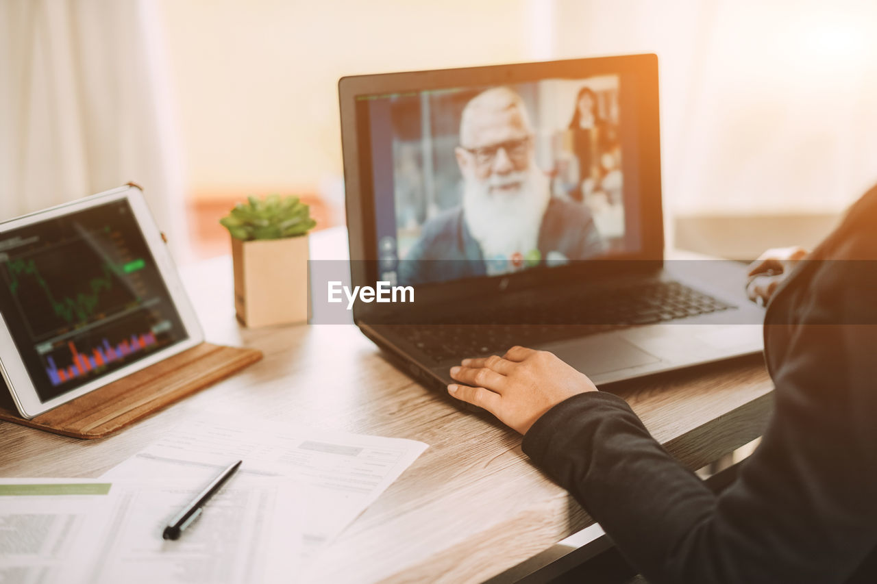 Midsection of woman video conferencing over laptop on table