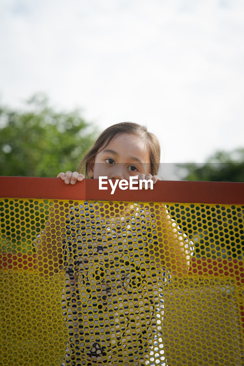 Portrait of a little girl with cute face holding fence and looking at the camera.