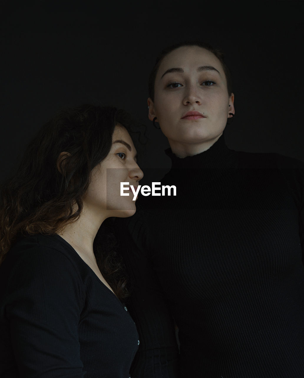 Portrait of sisters looking away against black background