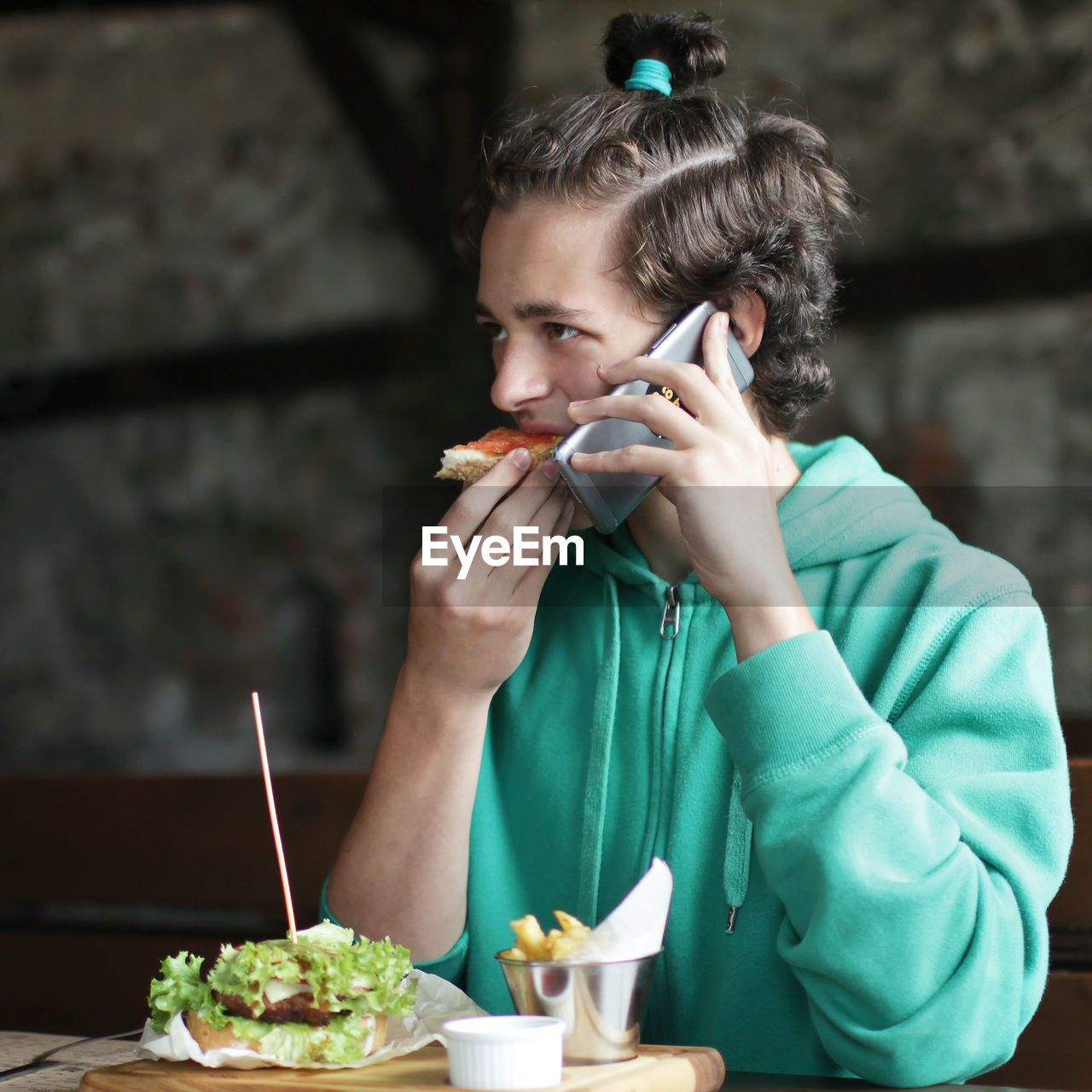 Young man eating food at restaurant while talking on phone