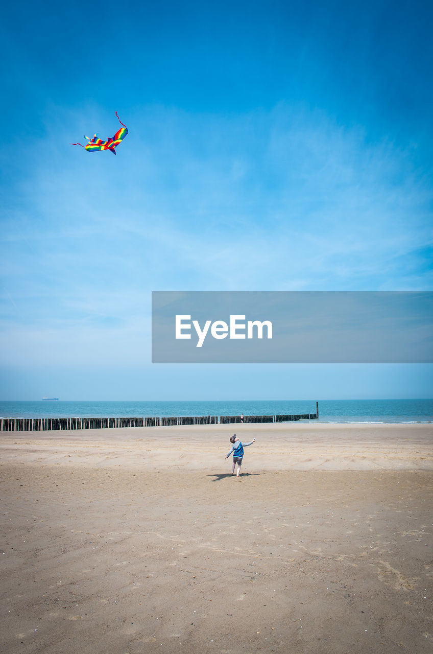 Rear view of boy flying kite at beach against blue sky