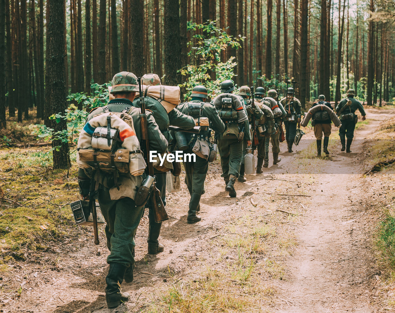 Rear view of army soldiers with equipment walking in row at forest