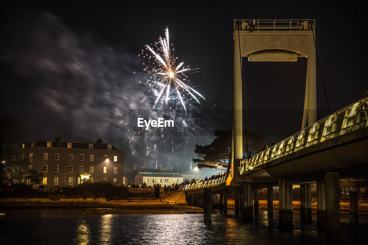 LOW ANGLE VIEW OF FIREWORK DISPLAY OVER RIVER AGAINST SKY