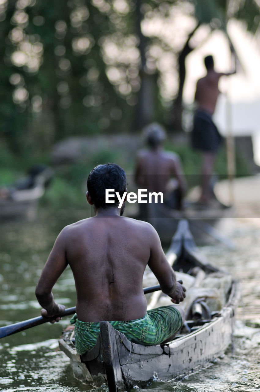 Rear view of shirtless man on boat at river