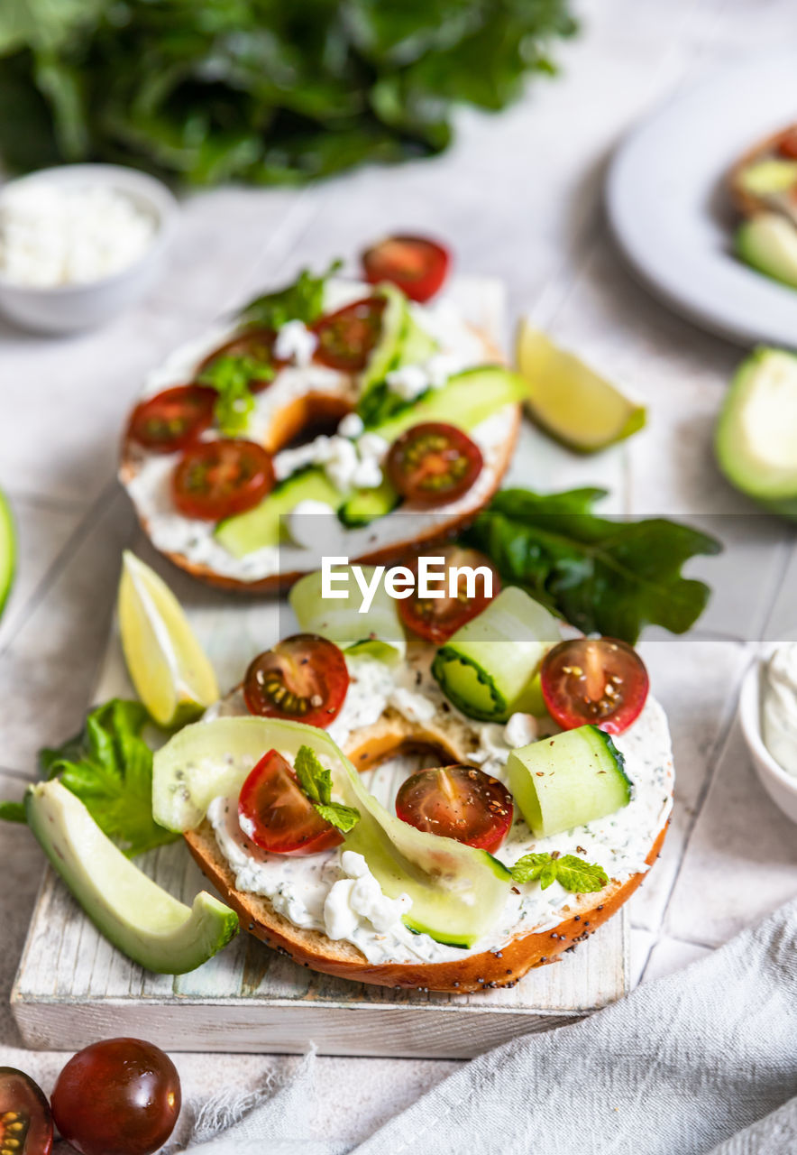 Bagels sandwich with cream cheese, cottage cheese, avocado, tomatoes, cucumbers and salad leaves