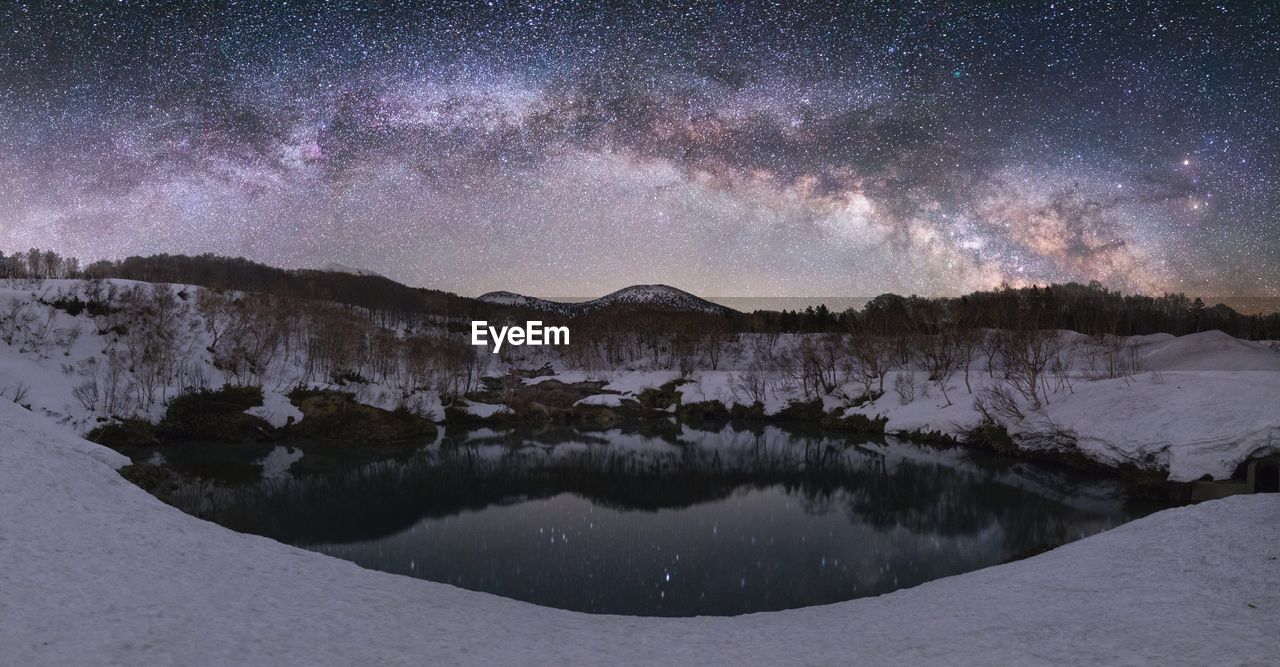 Scenic view of lake and mountains against star field during snowfall at night