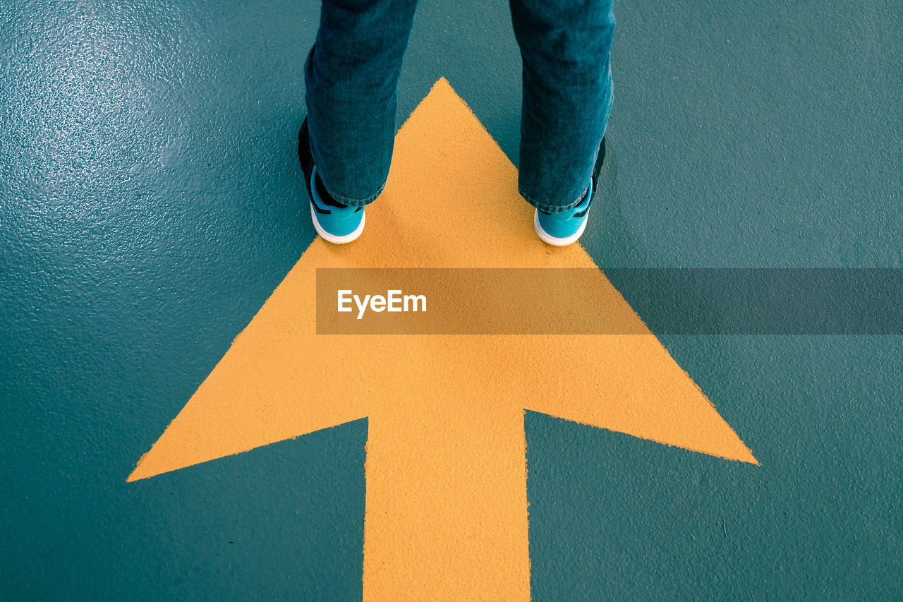 Low section of man standing on arrow sign