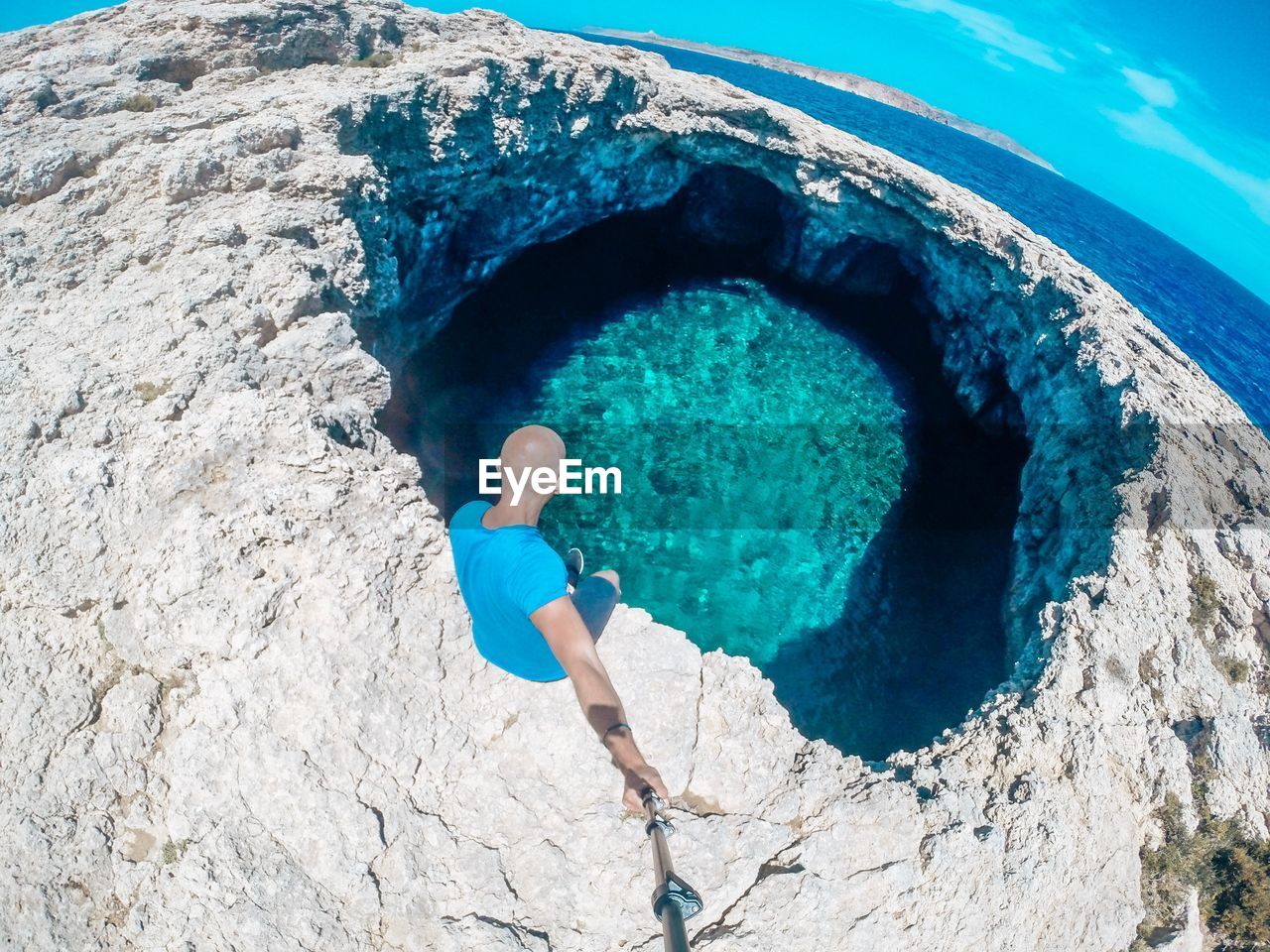 High angle view of man taking selfie while sitting by lagoon against sky