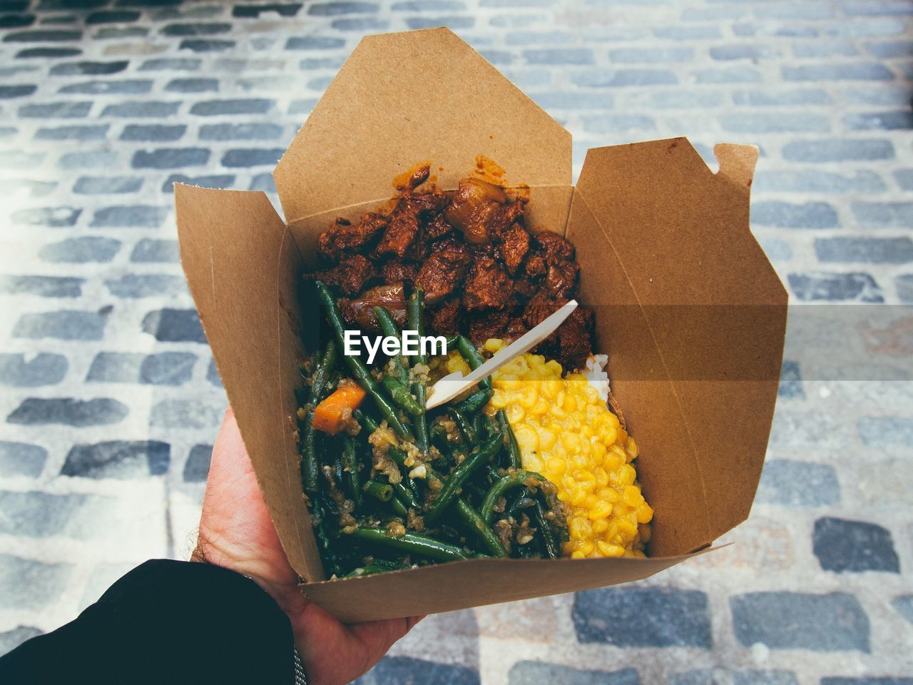 Cropped image of hand holding lunch in box on street