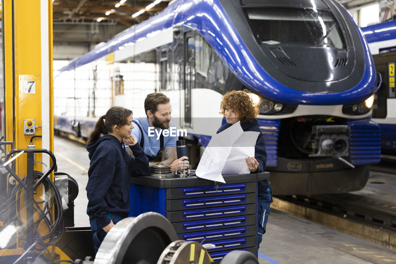 Trainees discussing with engineer over blueprint at factory