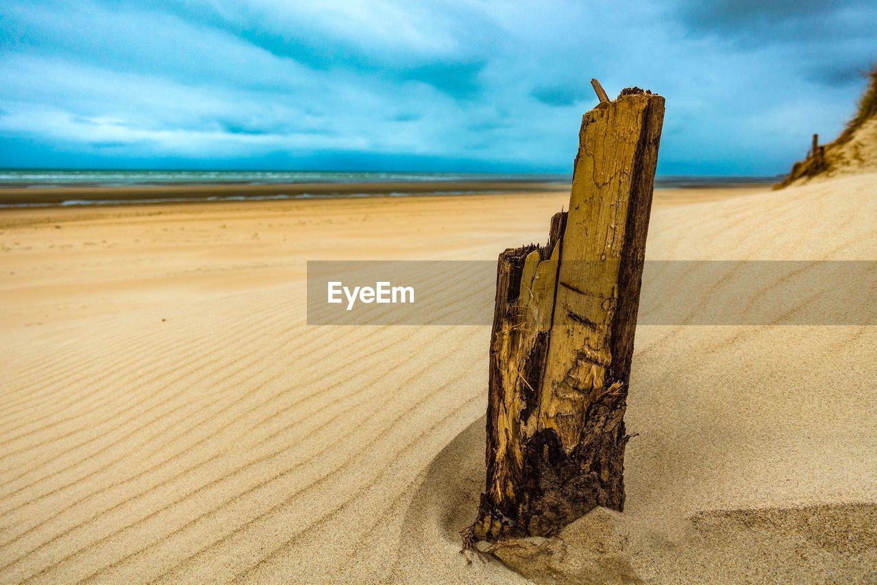 WOODEN POSTS ON SAND AT BEACH