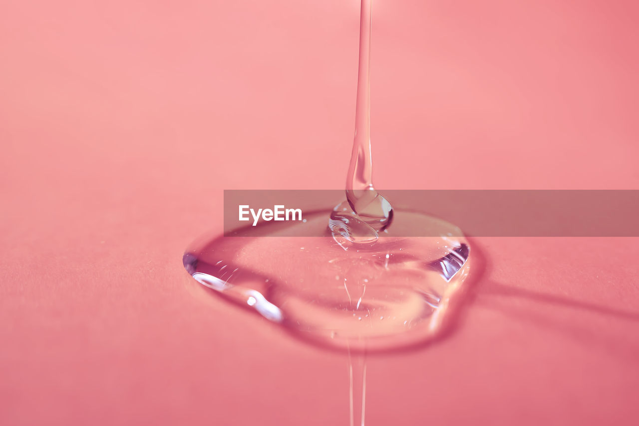 A drop of body gel or shampoo pouring from above on a pink saturated background.