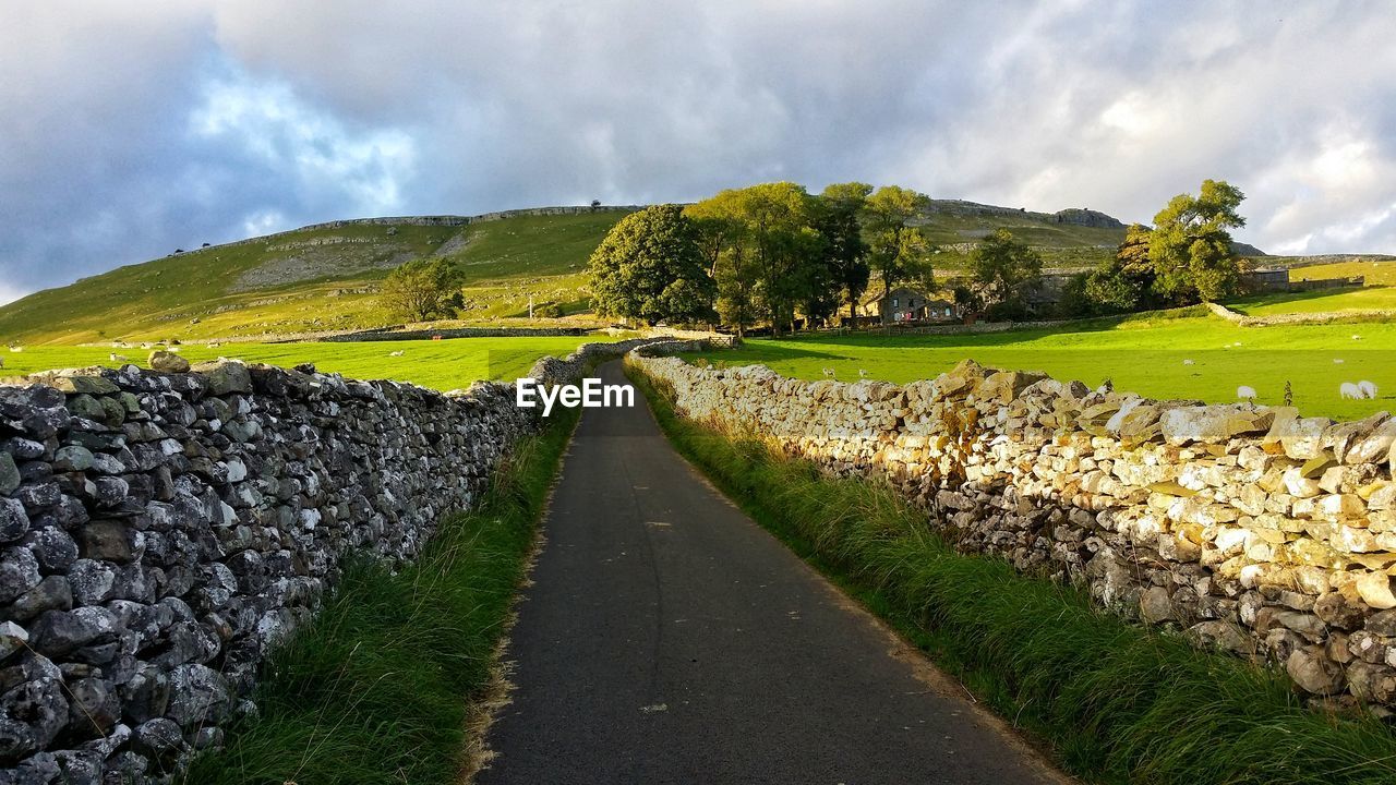 DIRT ROAD AMIDST LANDSCAPE AGAINST SKY