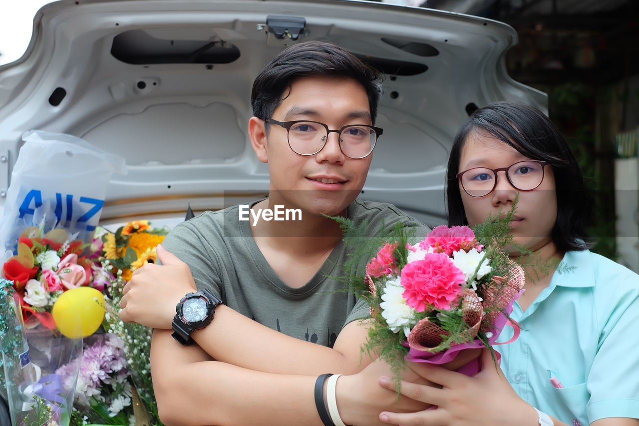 Portrait of siblings with bouquets sitting in car trunk
