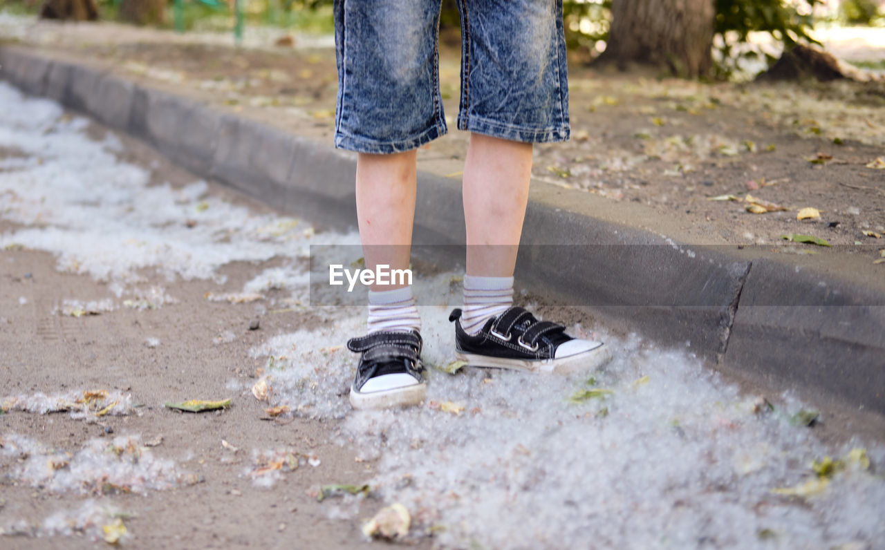 low section, human leg, one person, shoe, spring, limb, footwear, day, human limb, standing, casual clothing, lifestyles, leisure activity, nature, clothing, women, outdoors, yellow, child, footpath, adult, childhood, walking, plant, sneakers, jeans, fashion, selective focus