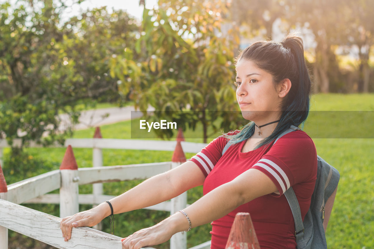 Beautiful young woman student, holding back with her two hands on a wooden fence, very happy 