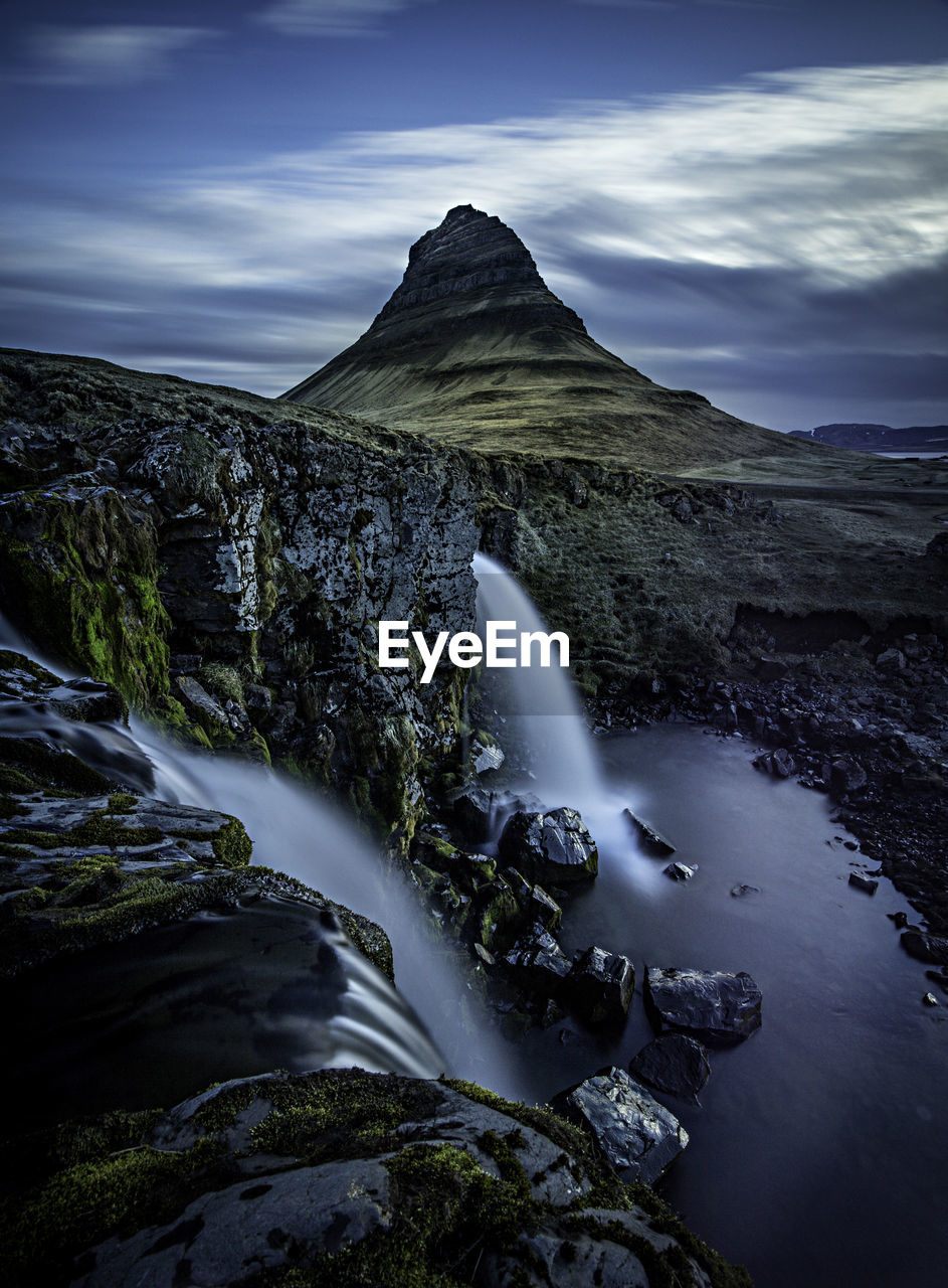 Scenic view of waterfall against cloudy sky