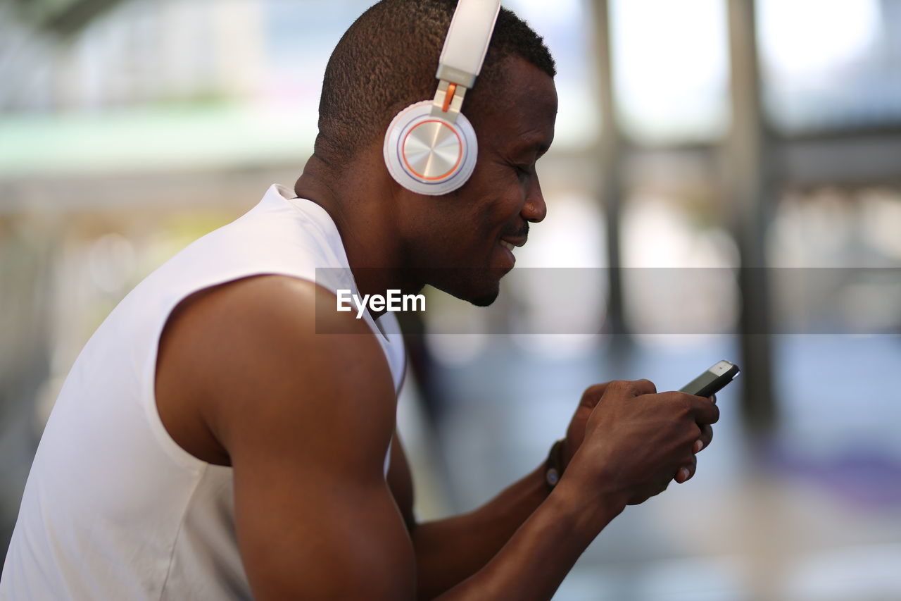 Smiling man using phone while wearing headphones