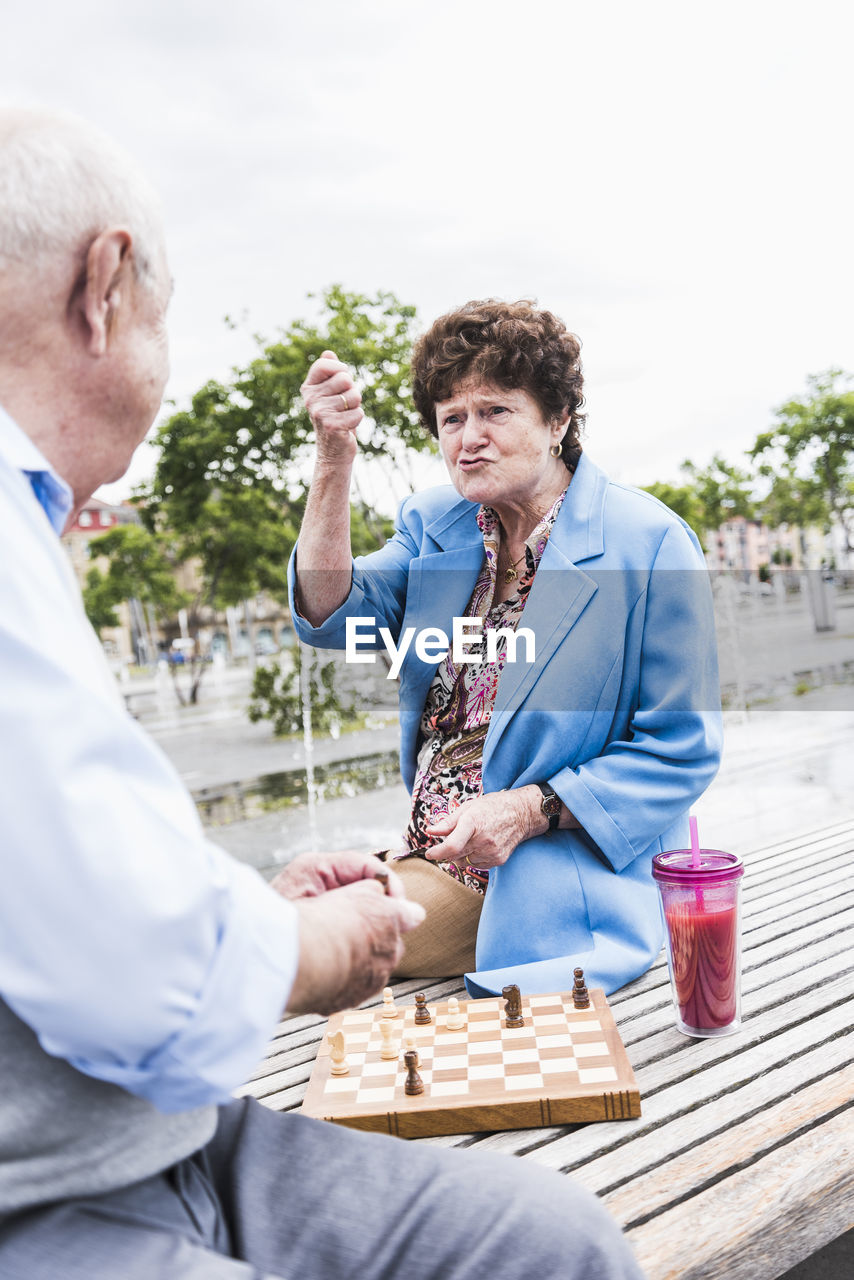 Portrait of senior woman sitting on a bench playing chess with her husband