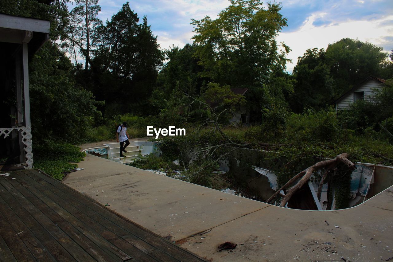 MAN STANDING ON RIVERBANK AGAINST TREES