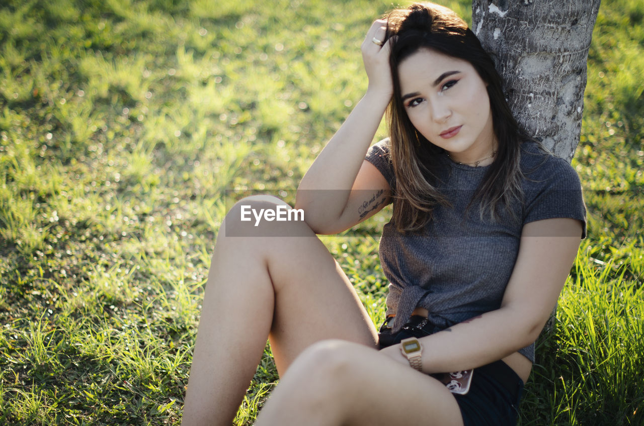 PORTRAIT OF BEAUTIFUL YOUNG WOMAN SITTING ON FIELD