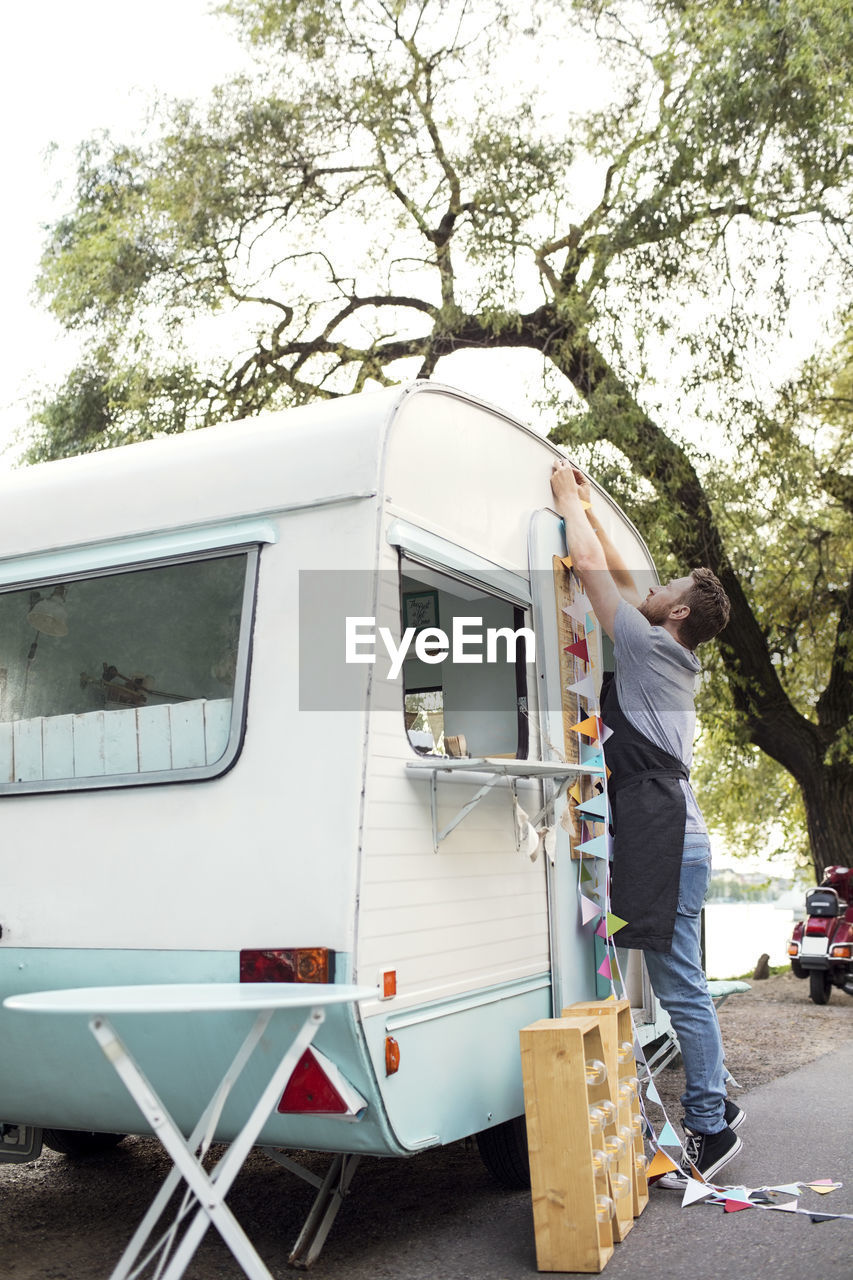 Full length side view of male owner hanging bunting on food truck