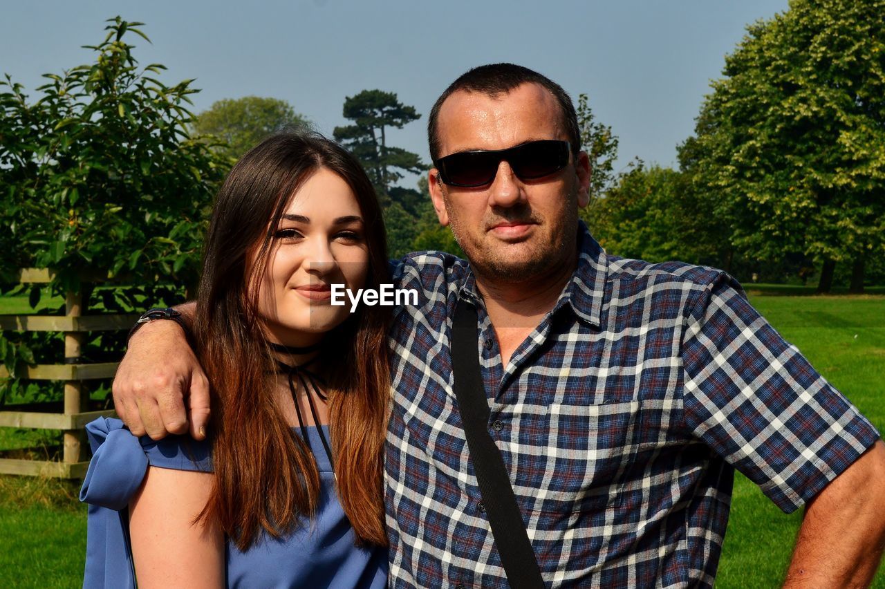 Portrait of couple standing at park on sunny day