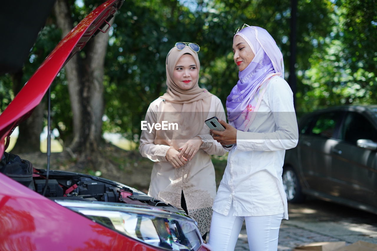 FULL LENGTH OF WOMAN STANDING ON CAR AGAINST THE WALL