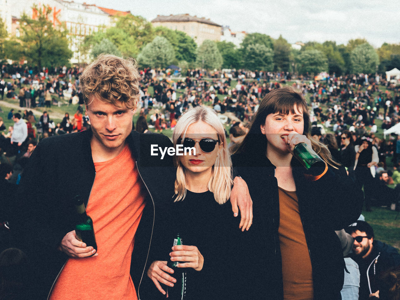 Portrait of young friends with beer bottle on field