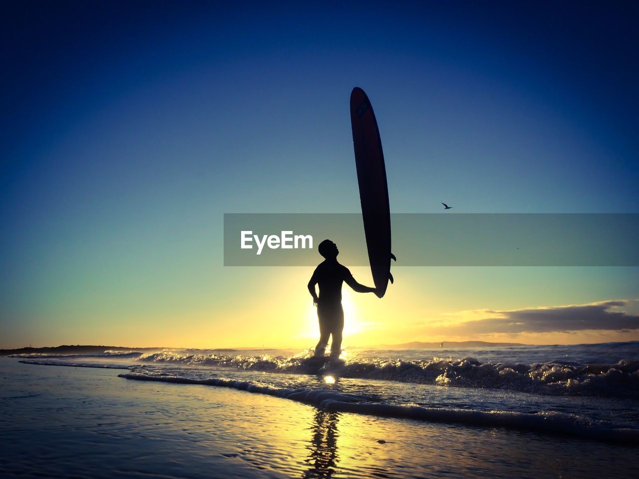 Silhouette man with surfboard on beach against clear blue sky