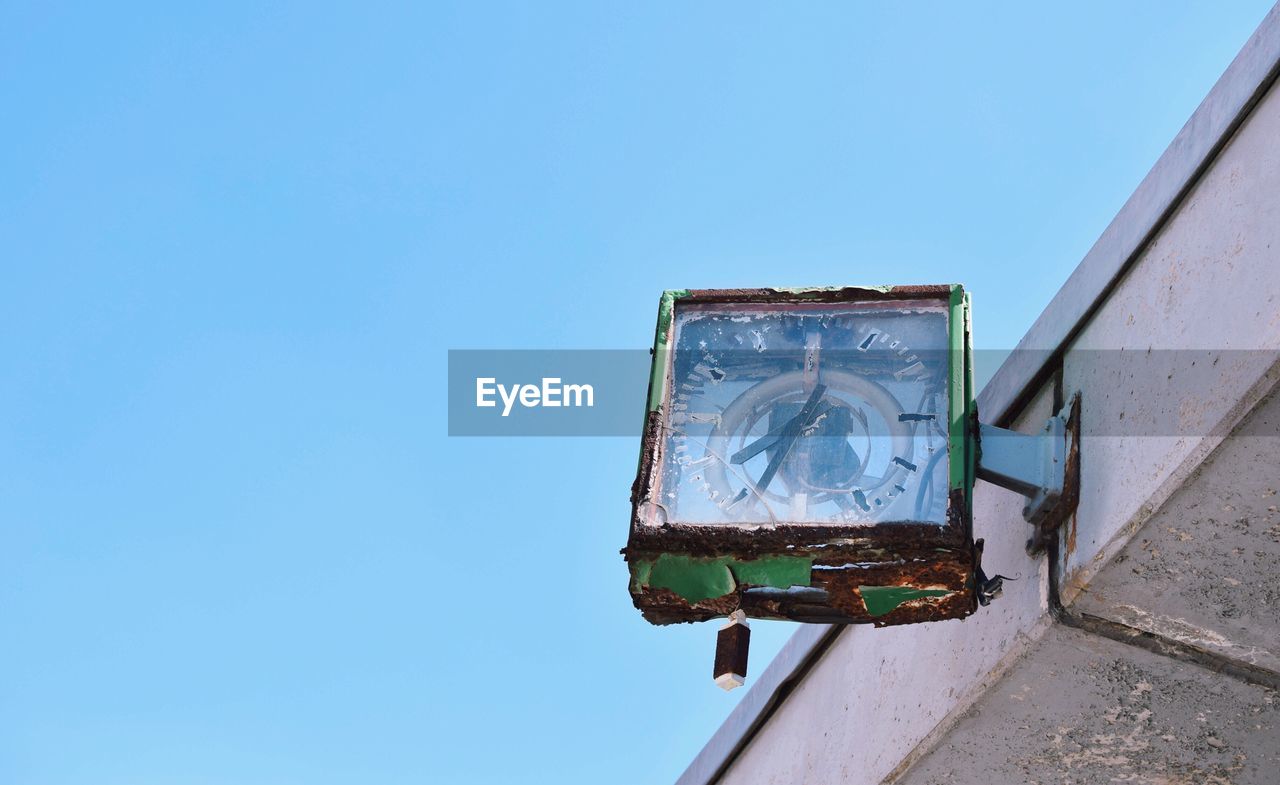 Low angle view of broken clock against clear blue sky
